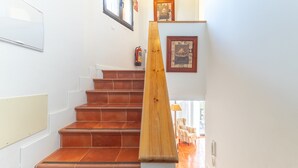 Una escalera con barandas de madera y piso de baldosas que conduce a una habitación con una silla y una lámpara.