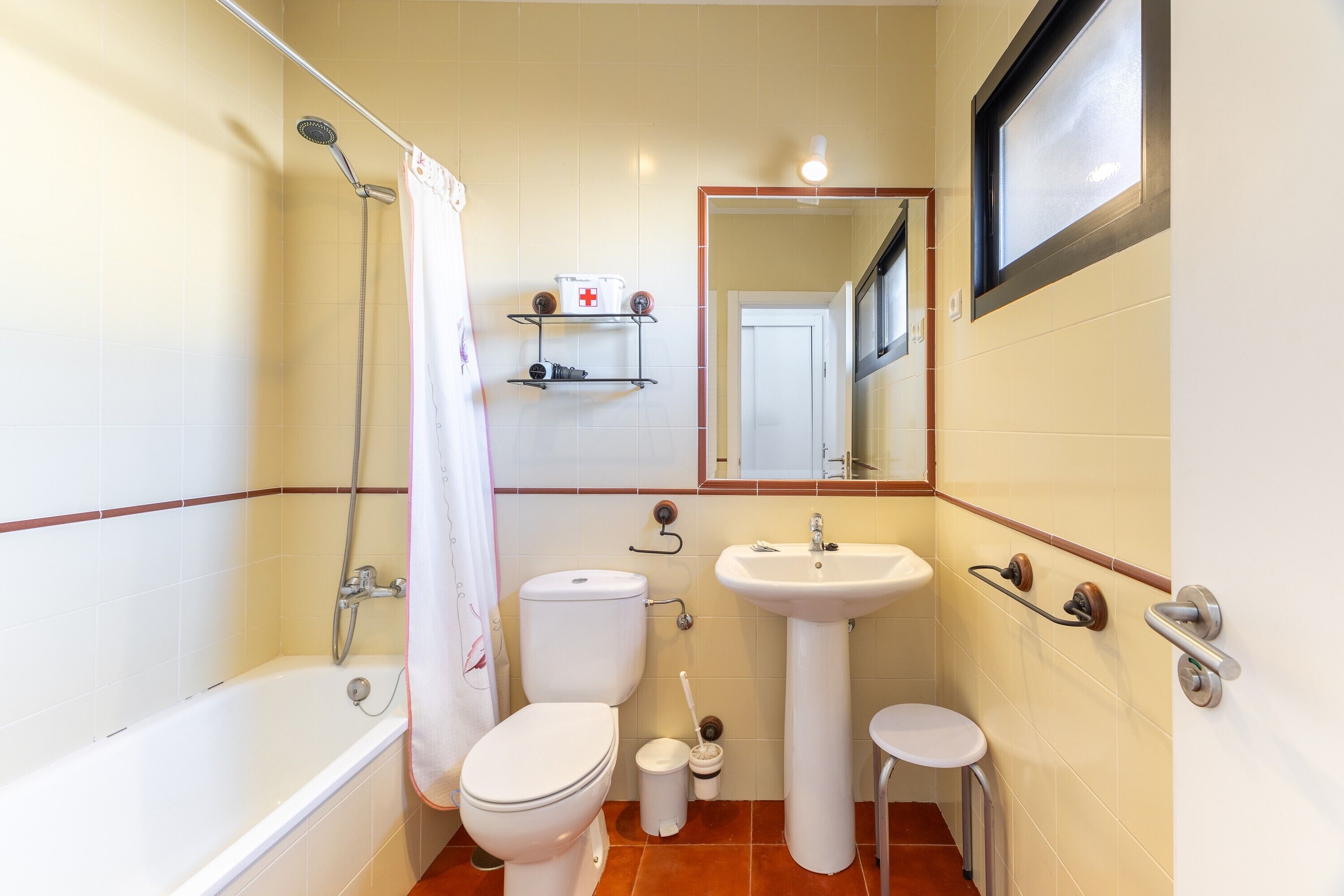 Un baño pequeño con bañera, inodoro, lavamanos y un taburete.