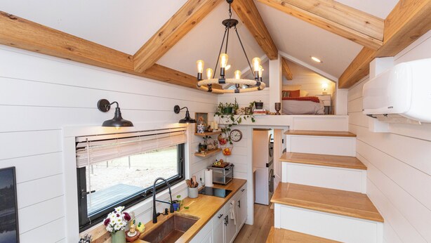 A compact kitchen with wooden beams, a hanging light fixture, and a window with blinds.