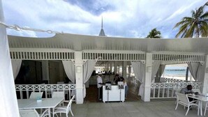 An outdoor seating area with white tables and chairs, a reception desk, and a view of the beach and palm trees. - Escape to the beach, live the luxury. Nueva Romana Beach. (San Pedro de Macorís)