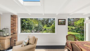 Ein Zimmer mit großem Fenster, das einen Blick auf einen Garten bietet, mit Kamin und Essbereich mit Tisch und Stühlen.