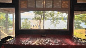 A room with a large window overlooking a lake, a checkered table, and a chair. - Welcome to the Wolf Den on Wolf Lake! (North Lawartha)