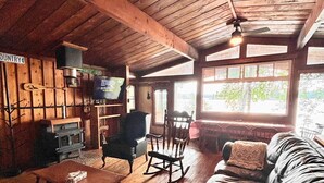 A rustic cabin interior with a wooden floor, a sofa, a rocking chair, and a fireplace. - Welcome to the Wolf Den on Wolf Lake! (North Lawartha)