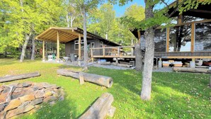 A cabin with a wooden deck, stone walls, and a covered outdoor area. - Welcome to the Wolf Den on Wolf Lake! (North Lawartha)