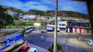 Una vista di una strada con un autobus, uno scooter e un'auto. Si vedono edifici e una collina sullo sfondo.