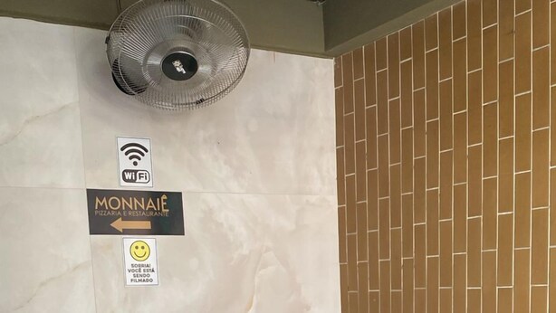 Un'area reception con il simbolo del Wi-Fi, la segnaletica di una pizzeria e ristorante Monnaie, un cartello con una faccina sorridente, una panca nera e un'esposizione di girasoli in vaso.