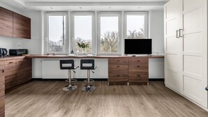 Una cocina moderna con un ventanal grande, dos taburetes de bar, un televisor de pantalla plana y armarios de madera.