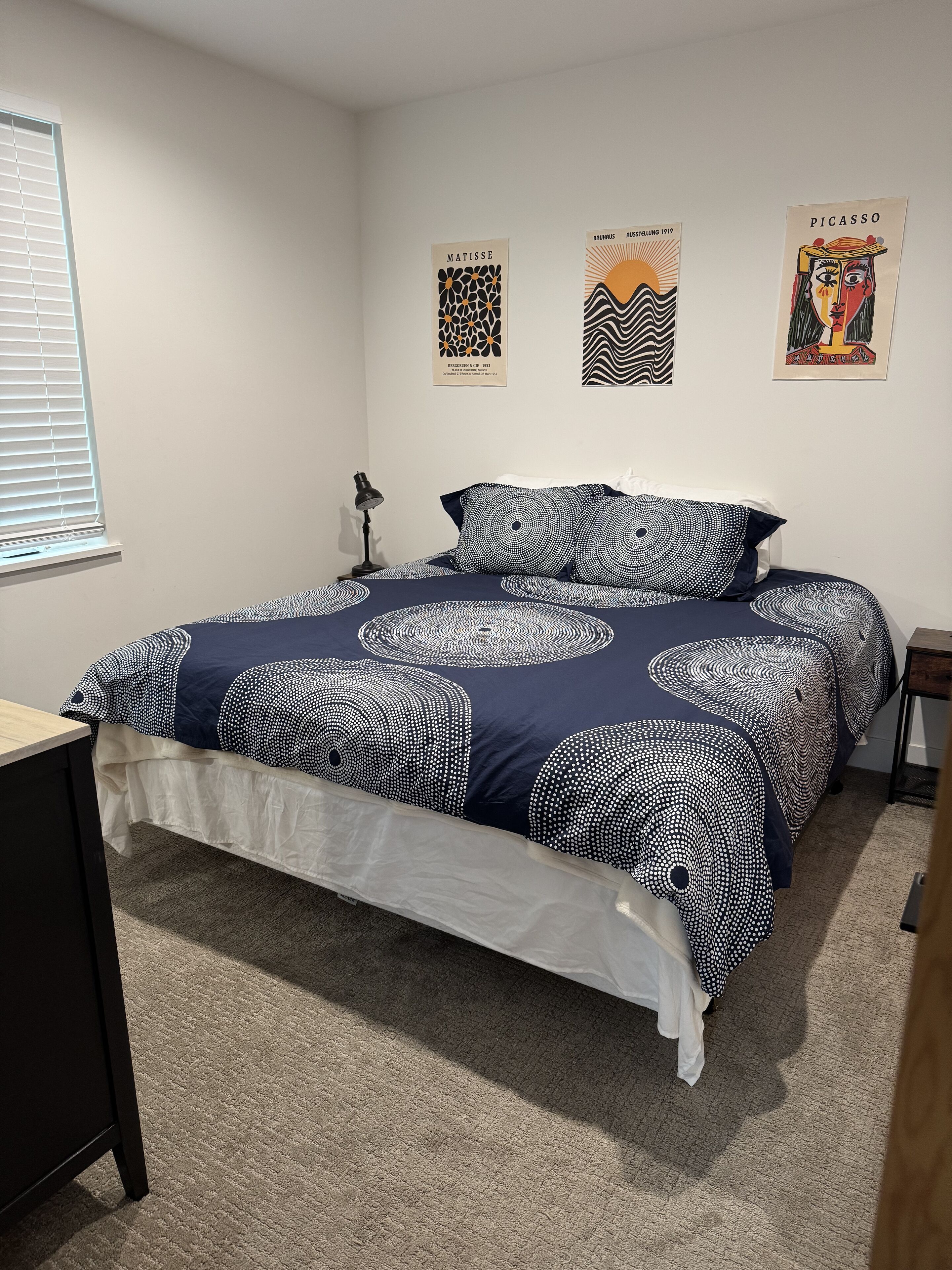 A bedroom with a bed, a desk, a lamp, and three wall art pieces.