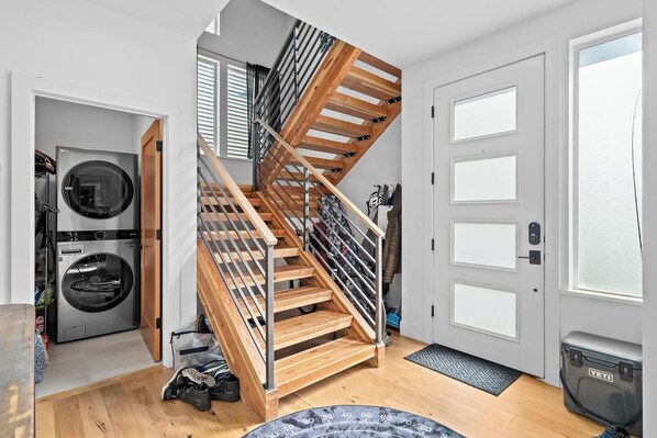 A modern apartment with a wooden staircase, a washing machine, and a YETI cooler.