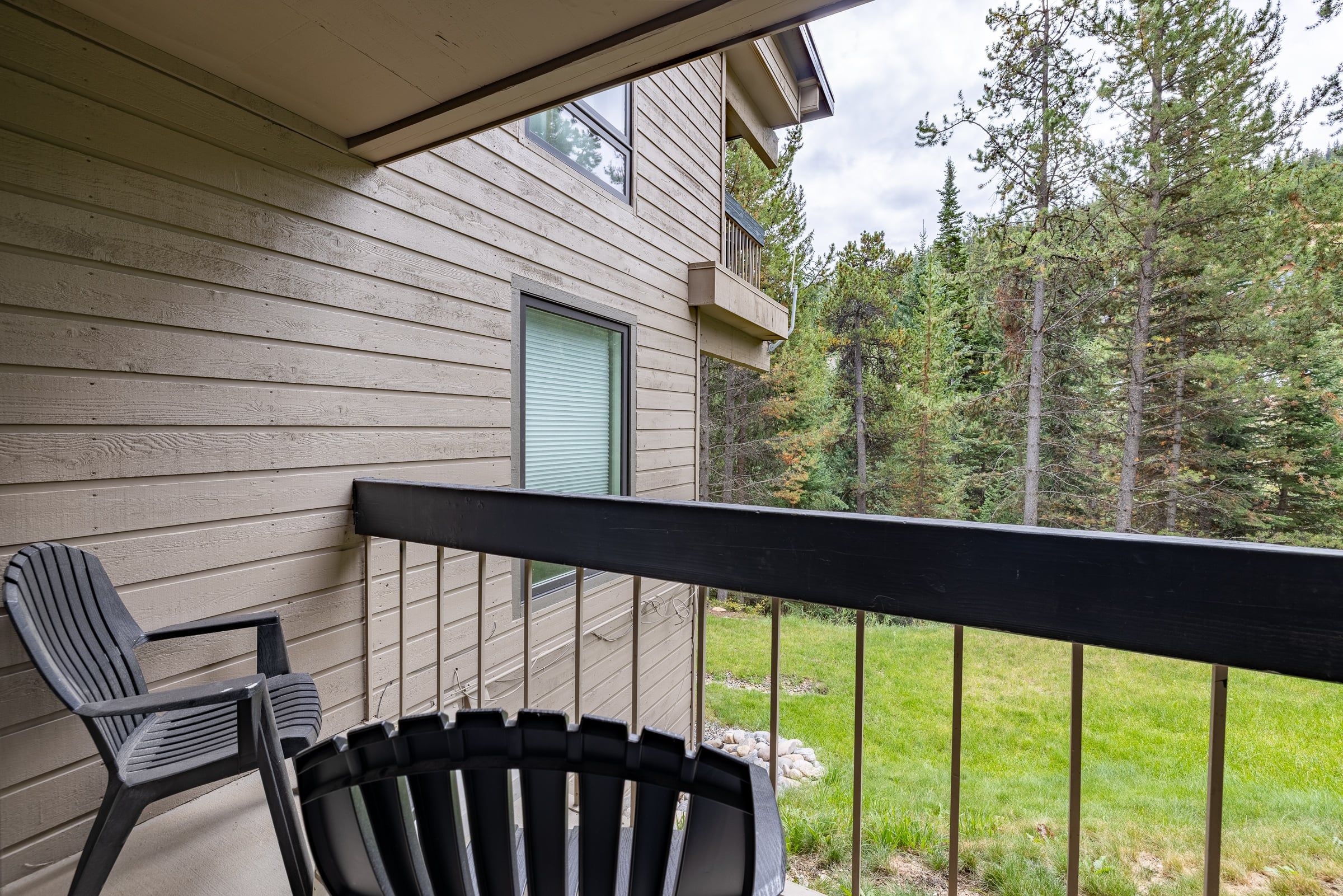 A wooden deck with a black railing, a chair, and a window with a closed shutter.