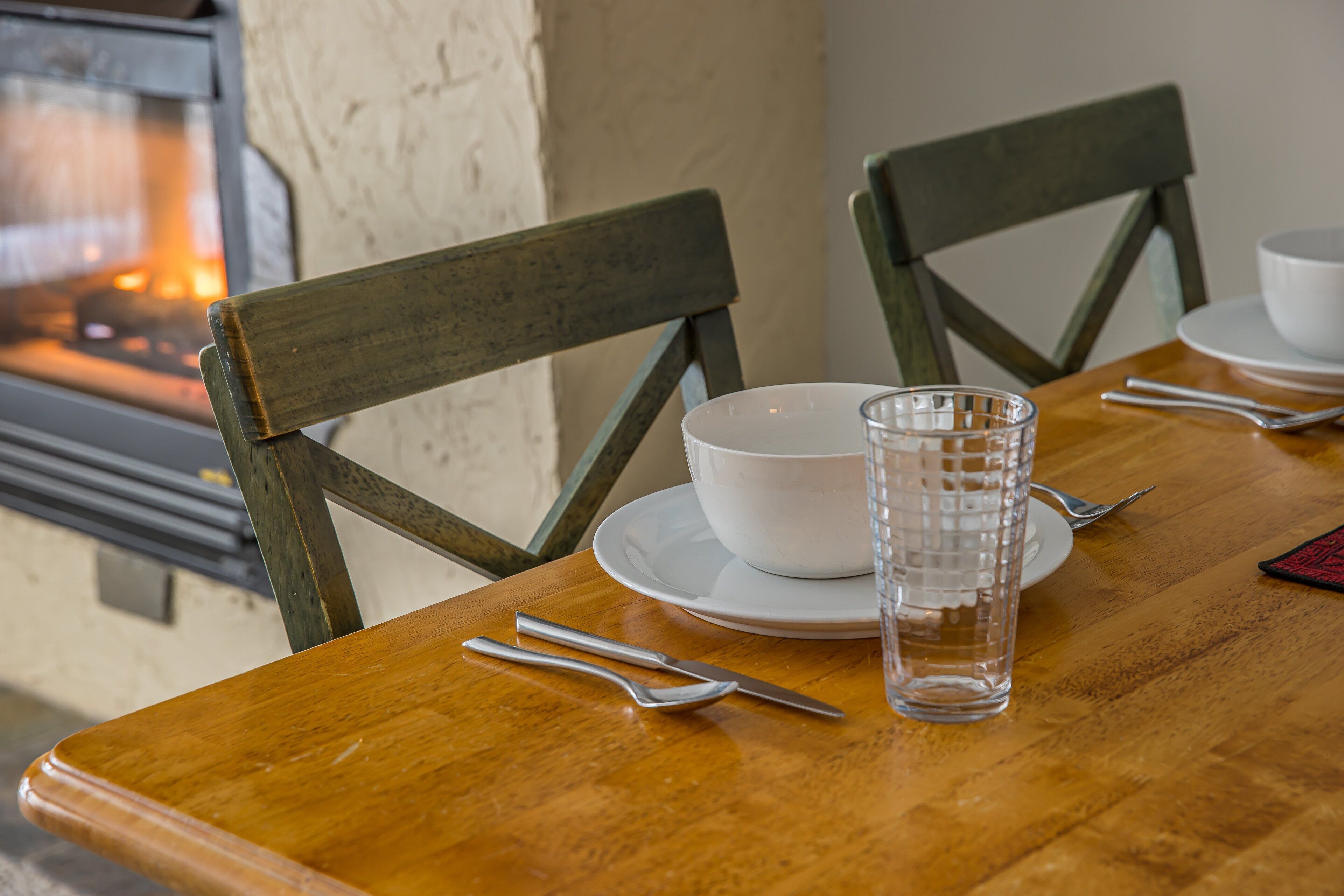 Une table de salle à manger en bois, avec un bol blanc, un verre et des couverts.