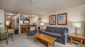 Een woonkamer met een grijze bank, een houten salontafel en een eethoek met een houten tafel en stoelen.