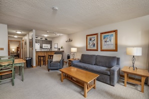 A living room with a grey sofa, wooden coffee table, and a dining area with a wooden table and chairs.