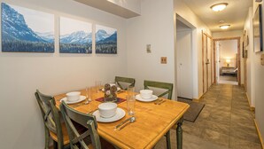 Een eetgedeelte met een houten tafel voor vier personen, stoelen en drie berglandschappen in lijstvorm aan de muur.