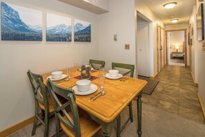 A dining area with a wooden table set for four, chairs, and three framed mountain landscape paintings on the wall.