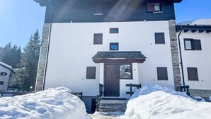 A two-story building with a white facade, a dark roof, and multiple windows. There is a snow-covered entrance and steps leading up to the door. - Rododendro by Interhome (Madesimo)