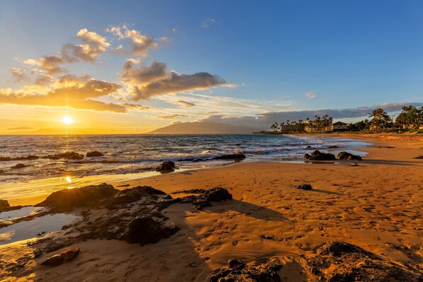 A beach with clear skies, ocean waves, and a distant mountain.