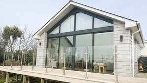 A modern house with large glass windows, a wooden deck, and a sloped roof.