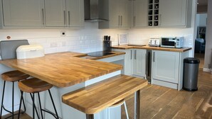 A modern kitchen with grey cabinets, a wooden countertop, a built-in oven, a microwave, and a trash bin.