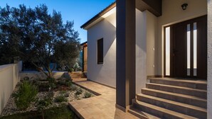 A modern house with a stone pathway leading to a dark wooden door, surrounded by a well-maintained garden with various plants and a small tree. - Villa Canziana (Istria - Pula) (Pula)