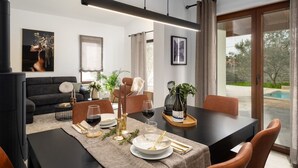 A modern dining area with a black table set for two, surrounded by brown leather chairs. A black sofa and a dining table with a beige placemat are visible in the background. - Villa Canziana (Istria - Pula) (Pula)