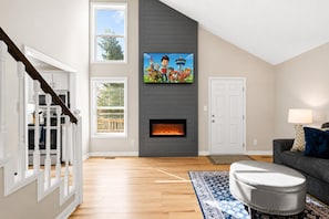 Una sala de estar con chimenea, televisor montado encima, una escalera y un sofá con alfombra.
