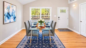 A dining area with a glass table, grey chairs, a blue patterned rug, a ceiling fan, and a door with a keypad lock. - Tranquil Retreat Near Lake Norman – Cozy, Spacious & Perfect for Relaxation! (Denver)