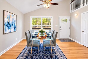A dining area with a glass table, grey chairs, a blue patterned rug, a ceiling fan, and a door with a keypad lock. - Tranquil Retreat Near Lake Norman – Cozy, Spacious & Perfect for Relaxation! (Denver)