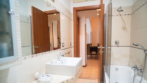 Un baño con lavamanos, espejo, ducha y una puerta que da a un comedor.