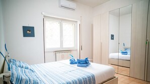 Un dormitorio con cama, ventana, radiador, armario y espejo.