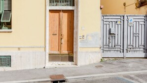 Entrada de un edificio con puerta de madera, repisa de hormigón, rejilla metálica y portón con un letrero.