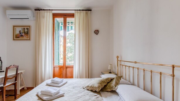 Un dormitorio con cama, escritorio, silla, ventana con cortinas y aire acondicionado instalado en la pared.