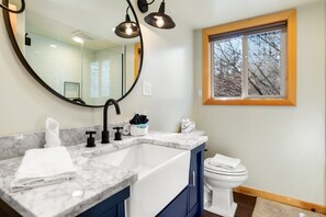 A bathroom with a marble sink, a large mirror, a toilet, and a window with a view of trees.