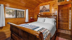 Un dormitorio de cabaña de madera con una cama grande, un ventilador de techo, una ventana con cortinas y una imagen de un oso en la pared.