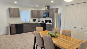 A modern kitchen with dark wooden cabinets, stainless steel appliances, and a dining area with a wooden table and chairs. - Hill Base Modern (Umatilla)