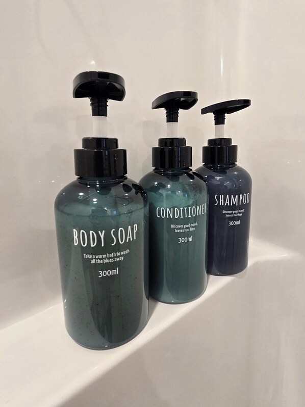 Three bottles of body soap, conditioner, and shampoo on a white shelf.