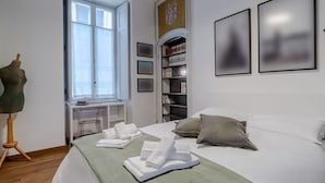 A hotel room with a bed, a desk, a chair, a wardrobe, and a window. - GuestHost - In the heart of Turin, in via Garibaldi, spacious apartment of 100 sqm in an elegant building from 1700. Accommodates up to 5 guests, located on the second floor with an elevator (steps to access it). In the city center, within the pedestrian (Torino)