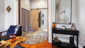 A room with a wooden floor, a patterned rug, a desk with a mirror, and a chair with a blanket.