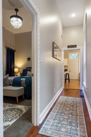 A hallway with a patterned rug, a chandelier, and a bed with a star decoration.