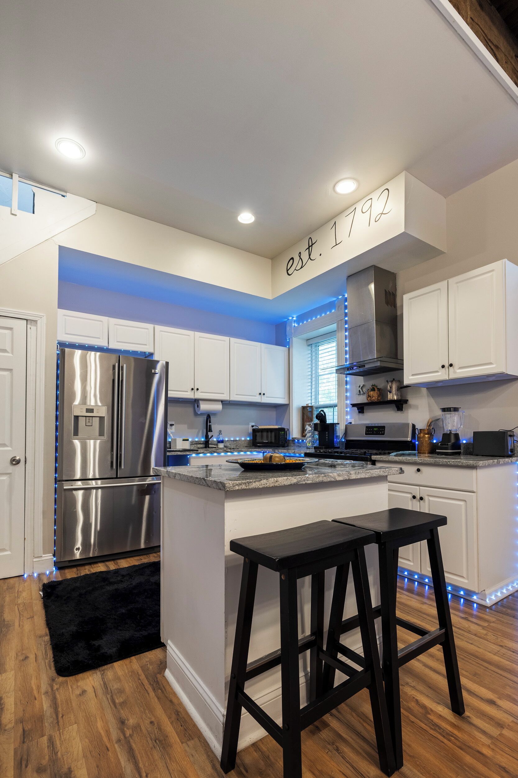 A modern kitchen with white cabinets, stainless steel appliances, and blue LED strip lighting.