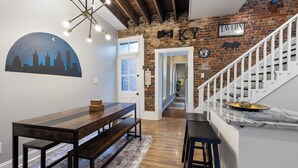A dining area with a wooden table and benches, a brick wall with a 'TAVERN' sign, and a staircase leading to another room.