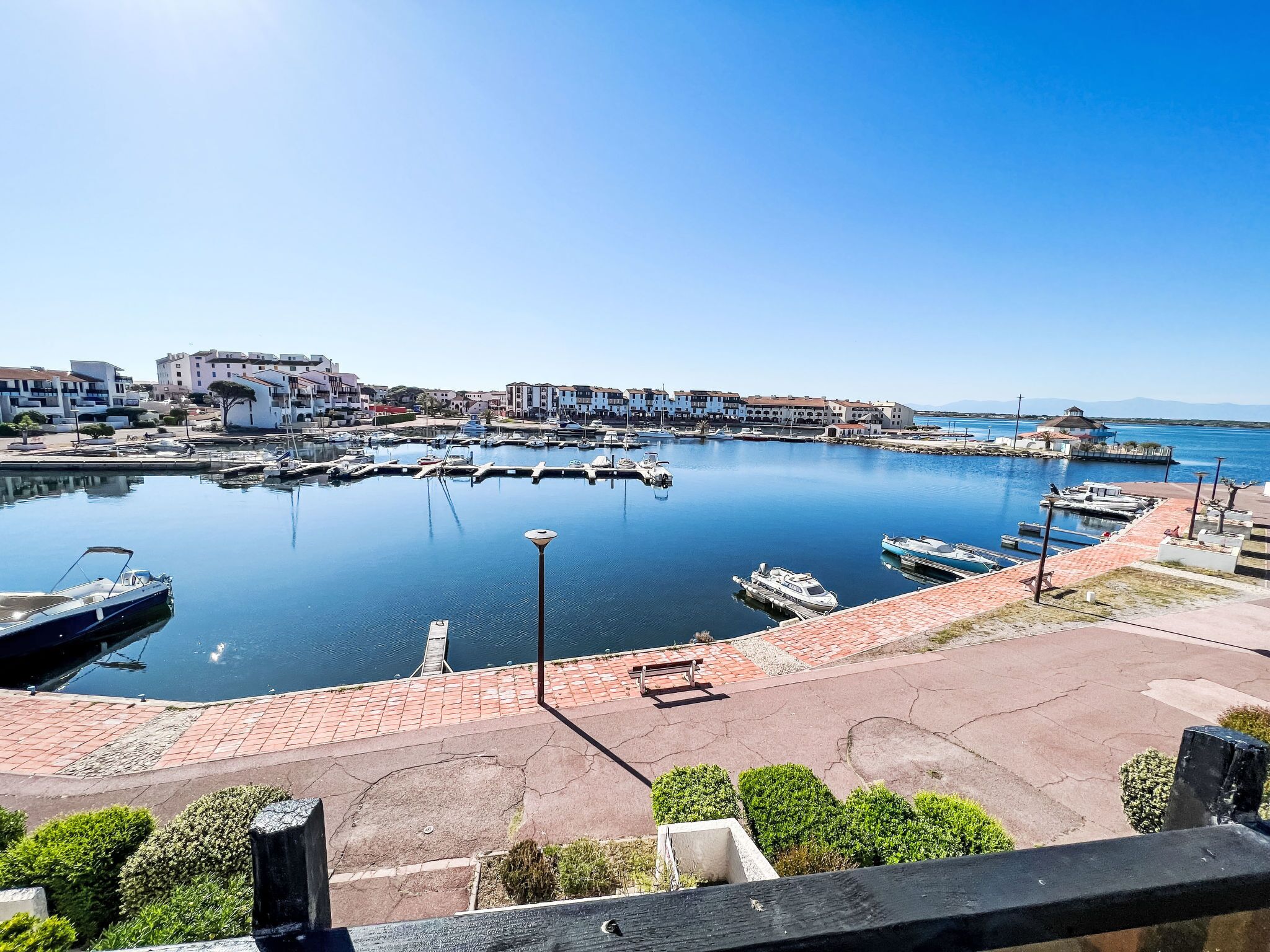 Un port de plaisance avec des bateaux amarrés, un ciel bleu dégagé et des bâtiments en arrière-plan.
