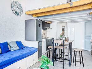 Un espace de vie compact comprenant un coin cuisine, un coin repas et un canapé avec des coussins bleus.