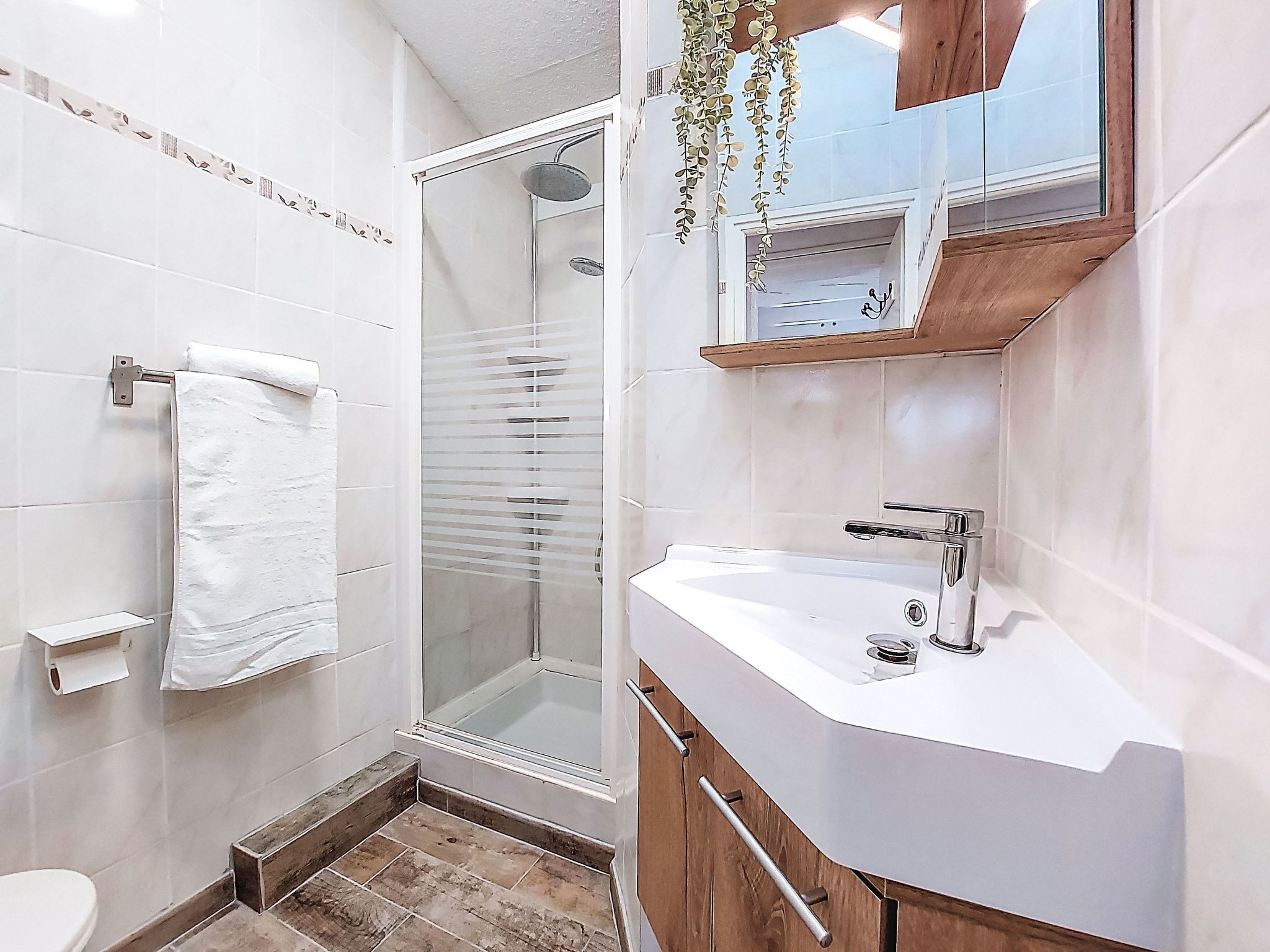 A bathroom with a shower, toilet, sink, and wooden cabinets.