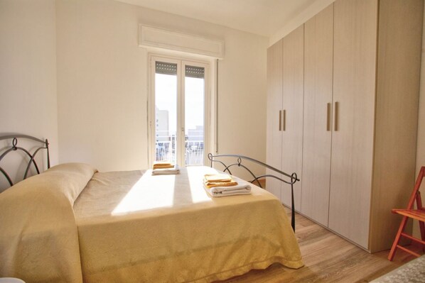 Une chambre à coucher avec un lit, une armoire, une fenêtre et une vue sur des immeubles.