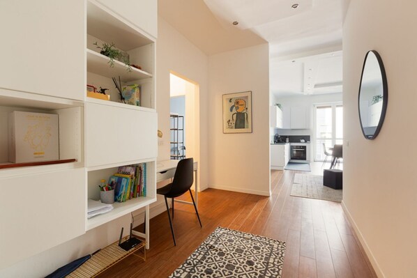 Un intérieur moderne avec un bureau, une chaise, une bibliothèque et, au fond, une cuisine.