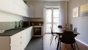 Une cuisine compacte avec des meubles blancs, un plan de travail noir et un coin repas comprenant une table et des chaises.