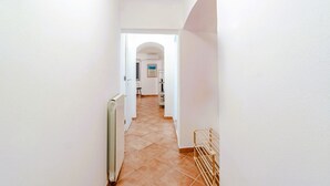 A narrow hallway with white walls and a tiled floor leading to a room with a door and a radiator. - GuestHost - In the heart of Genoa, on Via Rivoli, a cozy 60 sqm apartment ideal for 3 guests. Located on the -1 floor of a building without an elevator, it offers comfort and tranquility just steps from the lively city center. The area is well served by  (Genova)