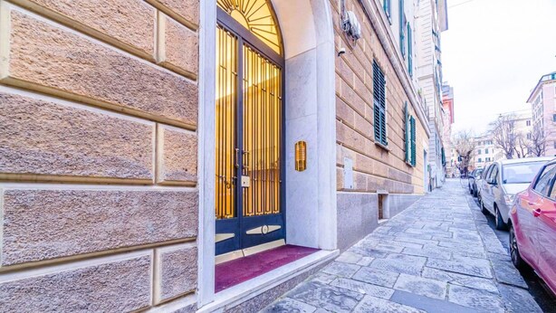 A building with a stone facade, a black door with golden accents, and a red carpet leading to the entrance. - GuestHost - In the heart of Genoa, on Via Rivoli, a cozy 60 sqm apartment ideal for 3 guests. Located on the -1 floor of a building without an elevator, it offers comfort and tranquility just steps from the lively city center. The area is well served by  (Genova)