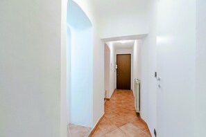 Un couloir étroit aux murs blancs et au sol carrelé, qui mène à une porte.
